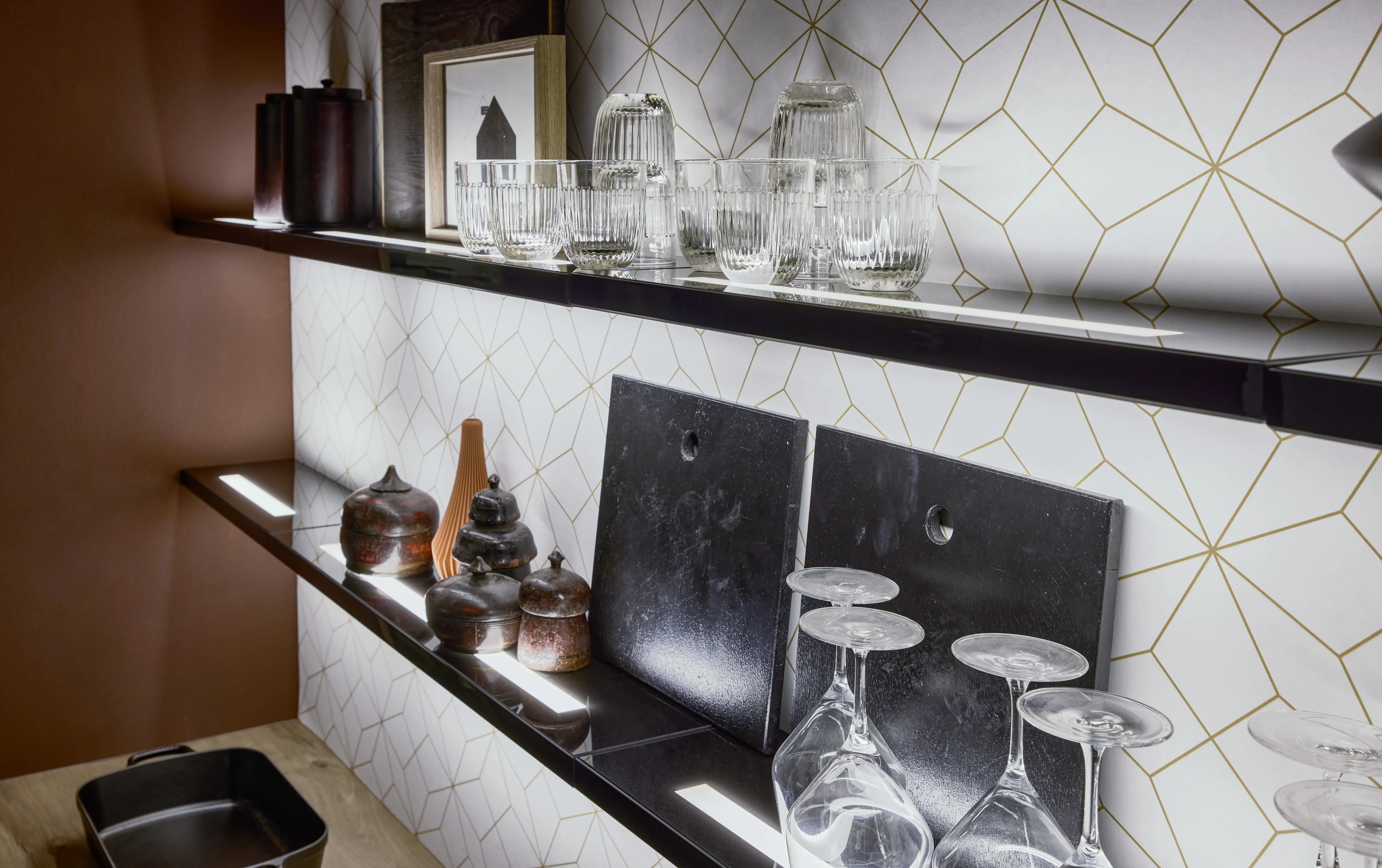 Zwei beleuchtete Regale mit Gläsern, Flaschen und Dekoration vor gemusterter Wand.