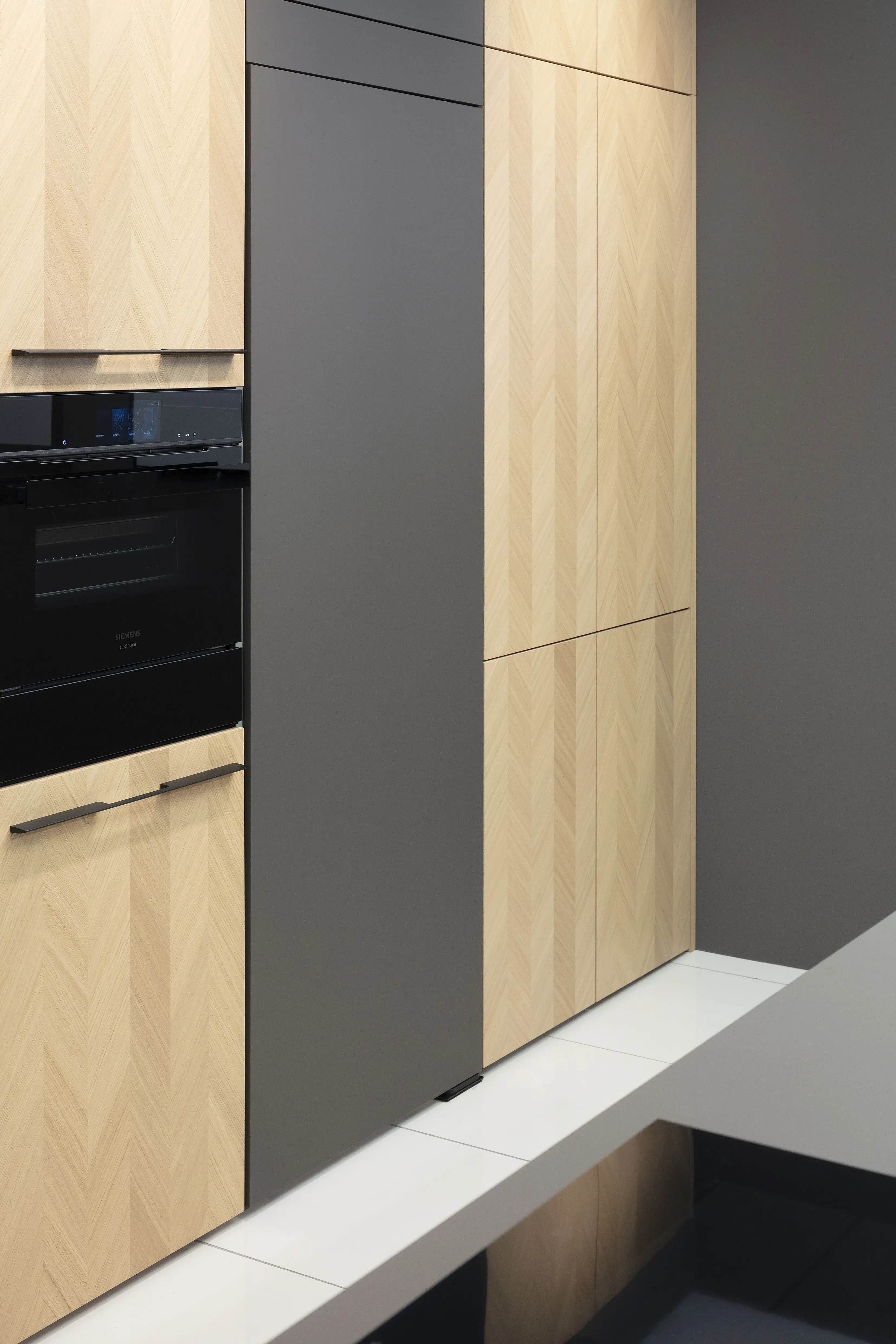 Front: Intarsia Gavi Eiche Furnier Resopal Brown Powder supermatt Korpus Schwarz APL: Resopal Brown Powder supermatt Geräte: Siemens Studio Line Spüle und Armatur: Blanco   Features: Front Echtholz Fischgrät-Optik, Kombination Echtholz und Resopal supermatt, Einbautür in Frontmaterial Resopal, Küchentheke Massivholz, APL = Korpusfarbe = Frontmaterial, Kombination Griffleiste und grifflos, Korpus in Frontmaterial, Wärmeschublade, Spüle und Armatur Schwarz, Besteckeinsatz. 